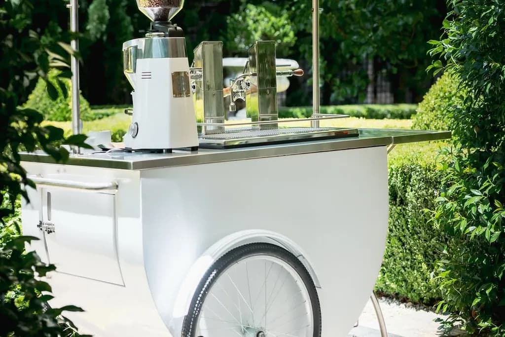 White coffee cart with a grinder and espresso machine in a garden setting